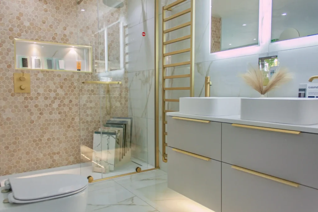 Modern bathroom featuring hexagonal tiles, double sink with gold accents, a glass-enclosed shower, and stylish lighting. Sleek, elegant design with neutral tones.